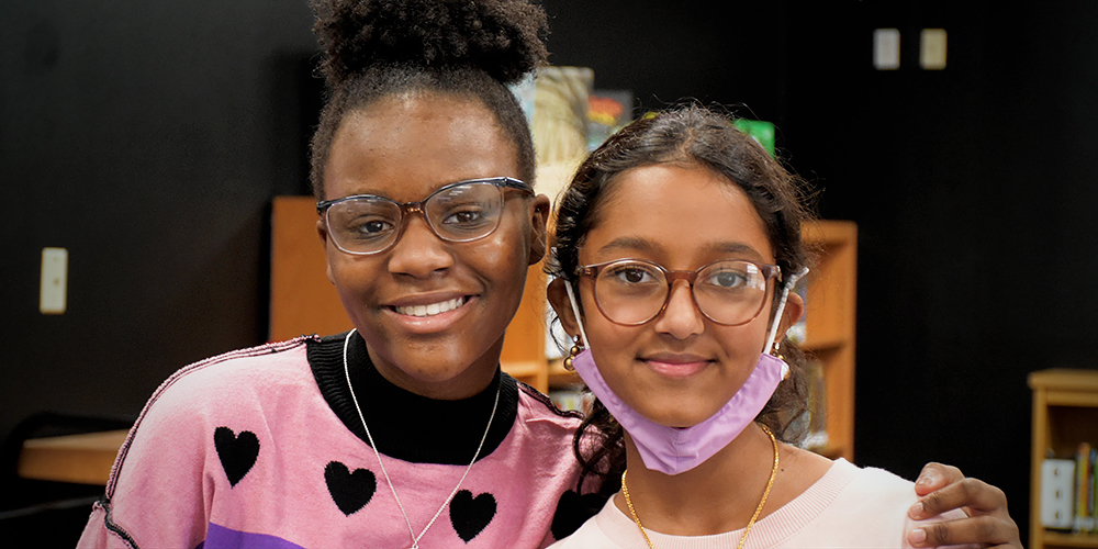 Two middle school students smile at the camera in the school library
