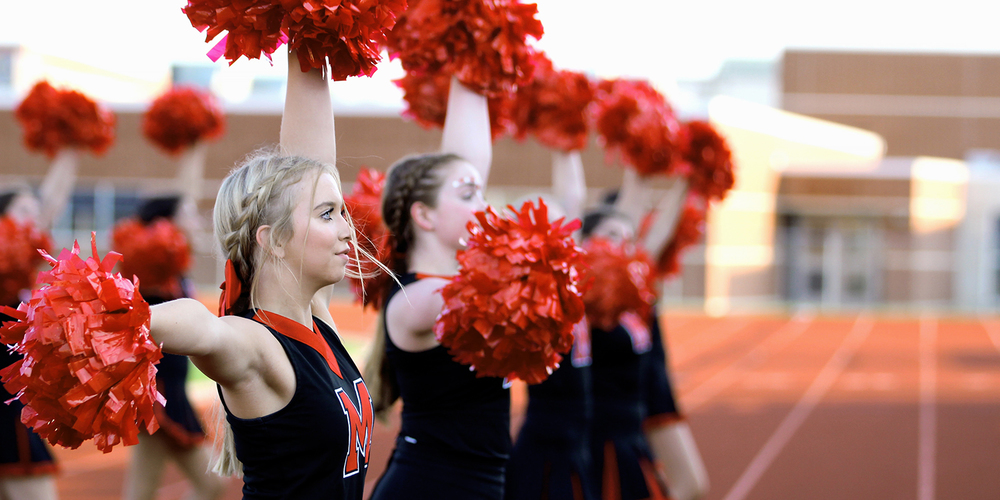 high school cheerleaders cheer from the sidelines at Cardinal Stadium