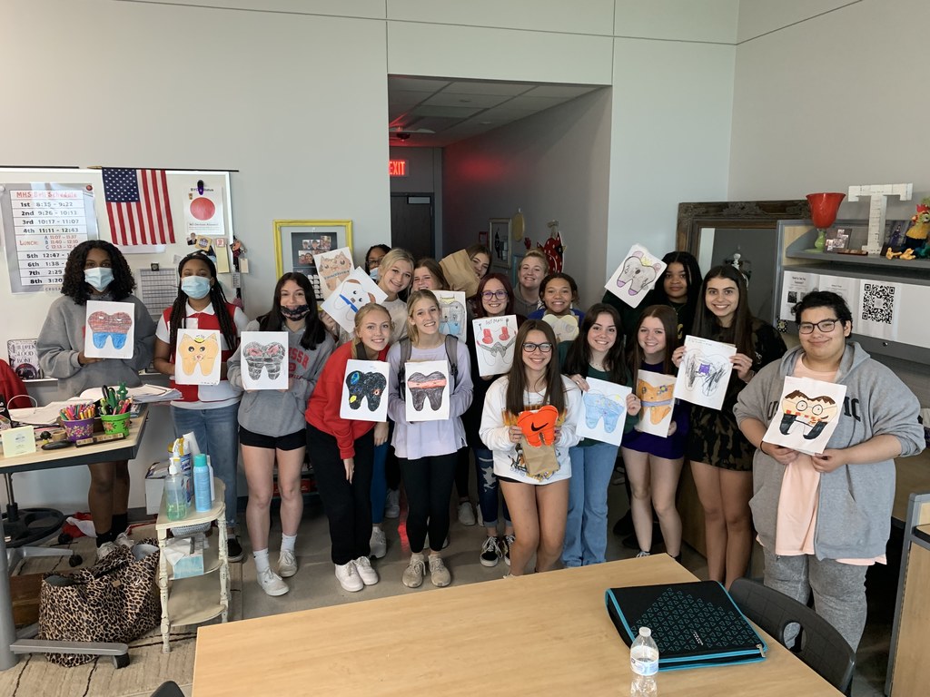 Fashion Design students hold up the tooth fairy pillow designs drawn by students in Mrs. Schneider's third grade class